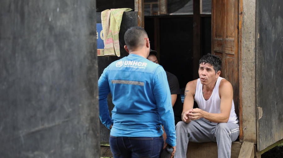 Owar, who fled Venezuela in search of a better life, sits on steps outside a shelter speaks with a UNHCR staff member.