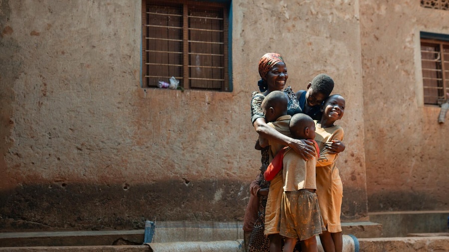 A Burundian woman hugs four of her children standing outside a building with a huge smile on her face
