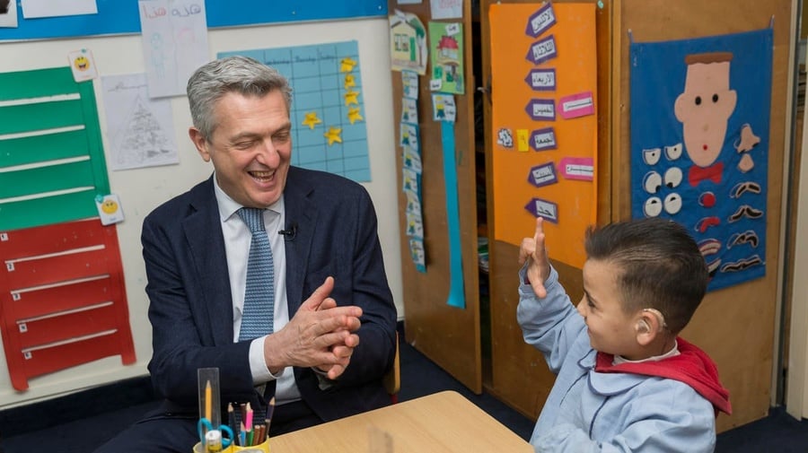 UNHCR High Commissioner Filippo Grandi sits with a 7-year old Syrian refugee child in a classroom. The child is wearing a hearing aid.