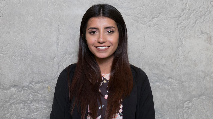 Portrait of a young woman standing against a grey background.