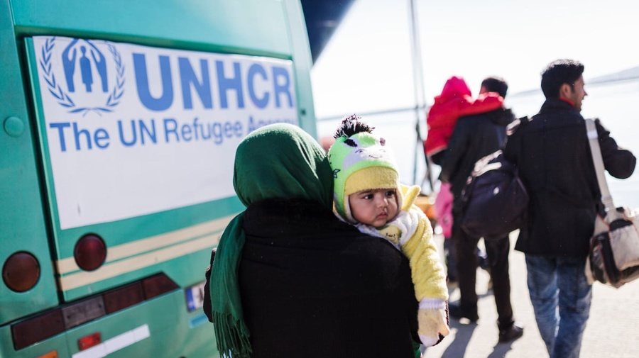 A woman carrying her young child walks towards a UNHCR bus.
