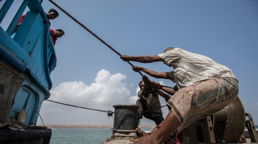 Men pull a rope to bring a boat into dock.
