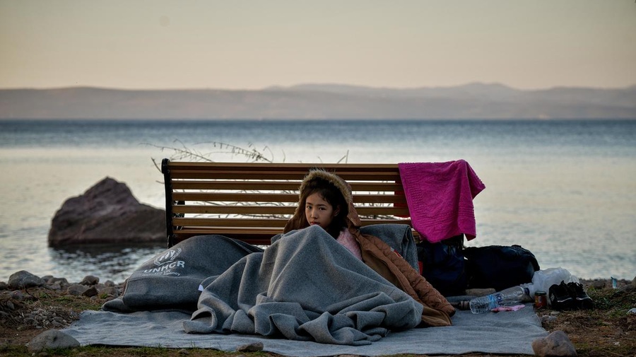 A young girl shelters with a blanket on the beach on Lesvos, Greece, March 2, 2020.