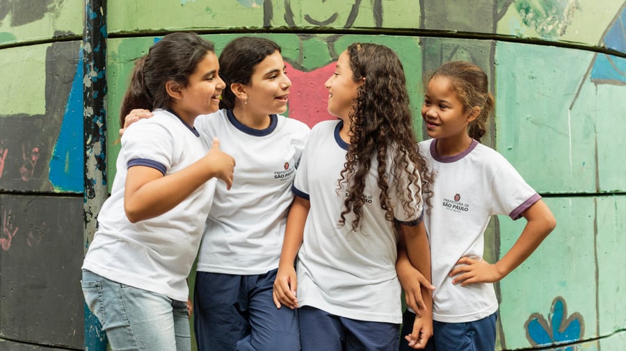 UNHCR UN Refugee Agency - How we do resettlement - ALT text: Four young girls enjoy chatting to each other while standing outside their classroom at the Duque de Caxias Municipal School in the Glicerio neighborhood of downtown Sao Paulo in Brazil. 