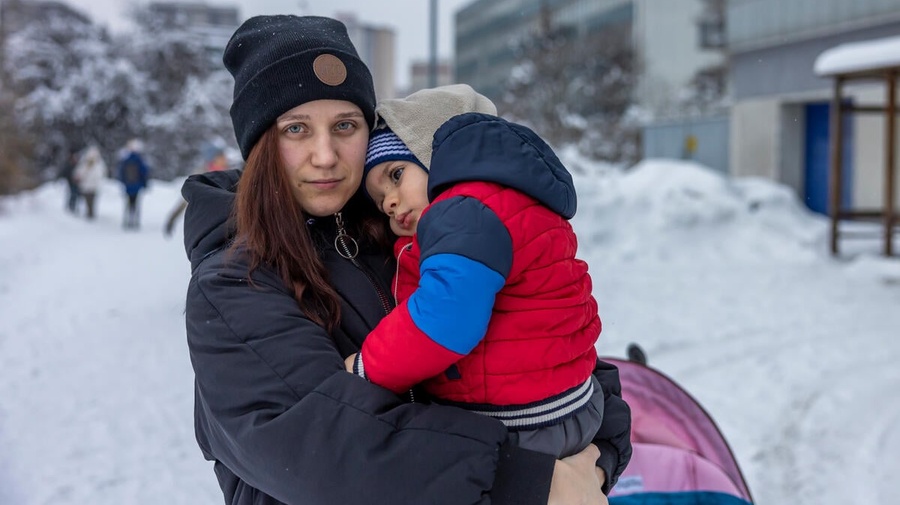 A woman stands outside in the snow holding a young boy.
